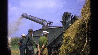 1971: farmers look on as a piece of farm equipment works through a pile of straw