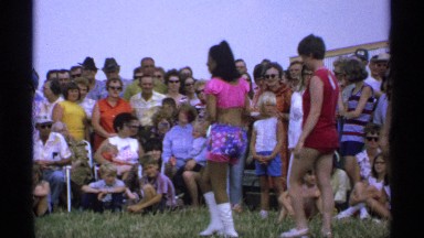 1971: seven women and one girl parade in front of a crown of men, women, and
