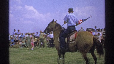 1971: a crowd of people watching a man holding an american flag while riding on