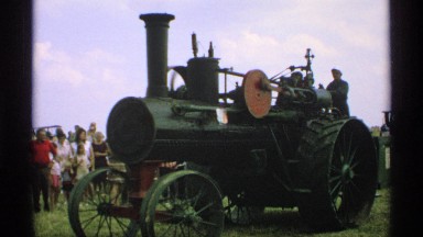 1971: standing men operate tractor from rear as parts move, spin and twirl