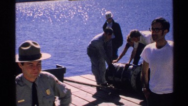1972: police and men rolling steel drum full of cement dockside; possible crime