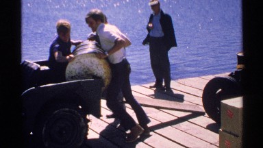 1972: three men loading a heavy oil barrel onto the back of a truck