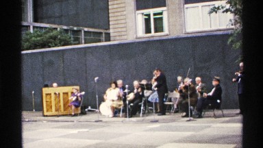1972: an old footage of musicians performing on a sidewalk in front of a wall