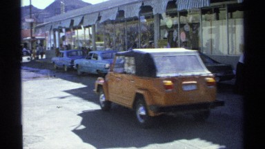 1975: car travels on the road and some building are at the right side at the