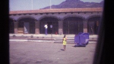 1974: woman walking on a windy day smiling at someone off screen with two men in