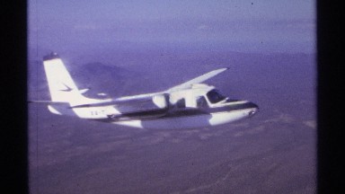 1974: a small airplane flying very high above a barren landscape, seen from