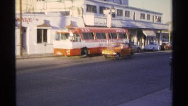 1975: orange vehicle drives up the street in nineteen fifties era, then parks