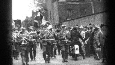 1937: a military band marching around a street corner while playing CLEVELAND