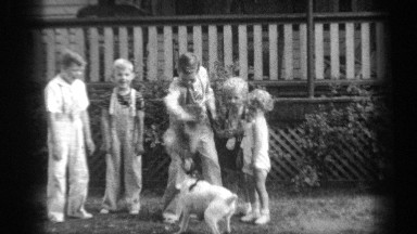 1938: group of six young people are happily standing outside playing with a dog