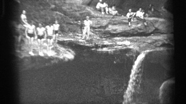 1938: man diving off rock with others in background near small waterfall