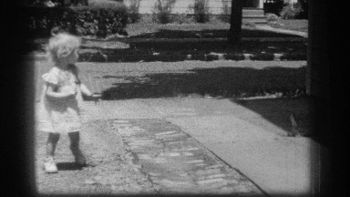 1939: a female child walks alone in the street holding a lollipop and she turns