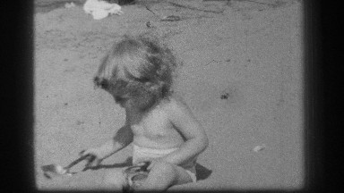 1939: a toddler looks around and plays on a sandy beach in the sunshine