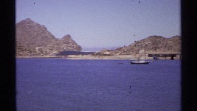 1974: small boats are in the sea close to the shore where are mountains. CABO