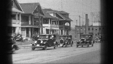 1937: vehicles from bygone era driving down the street with their drivers waving