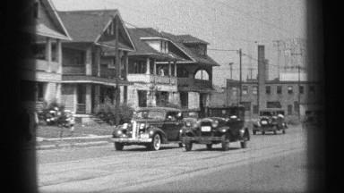 1937: cars are running beside a residential area where few women, childs are