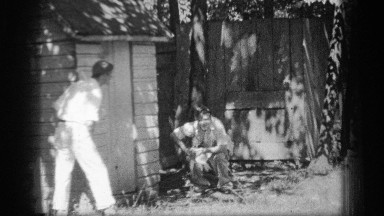 1937: man pooping behind a shed while another keeps watch CLEVELAND OHIO