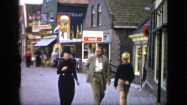 1957: An old couple walk in the street with a blonde child, where other people