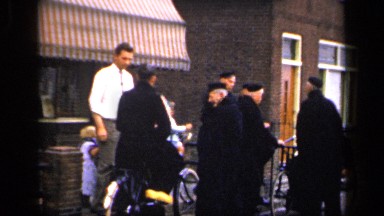 1957: Man in Street Clothes Talks to Men in Black Caps and Outfits