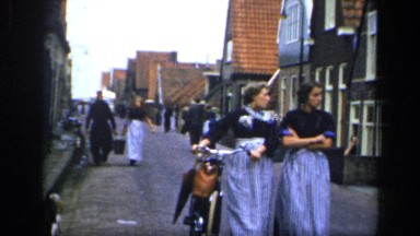 1957: people are walking with cycle in a residential area where some stray dogs
