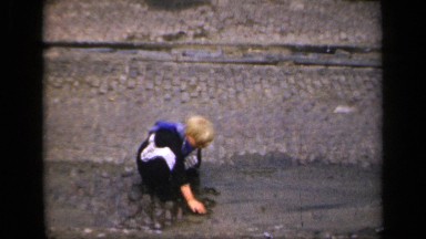 1957: Young Male Child Plays with Rocks in a Puddle and Has Fun