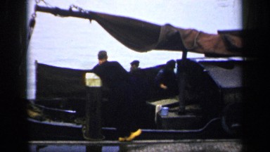 1957: three people are talking inside the boat and it located at the water at