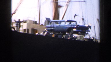 1957: A Ship's Crane Lowering a Car onto a Platform Below England