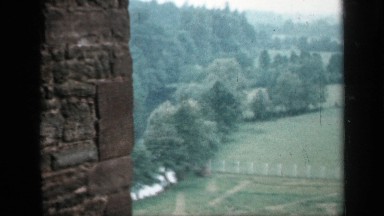 1957: panning view of a field from behind a stone wall, with a farmhouse and