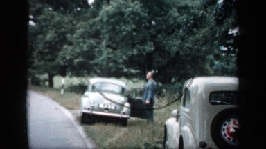 1957: two cars parked on the grass by the side of the road, with one of the