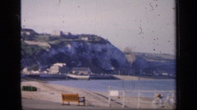 1957: bicycles lean against long railing at beach across from steep cliff