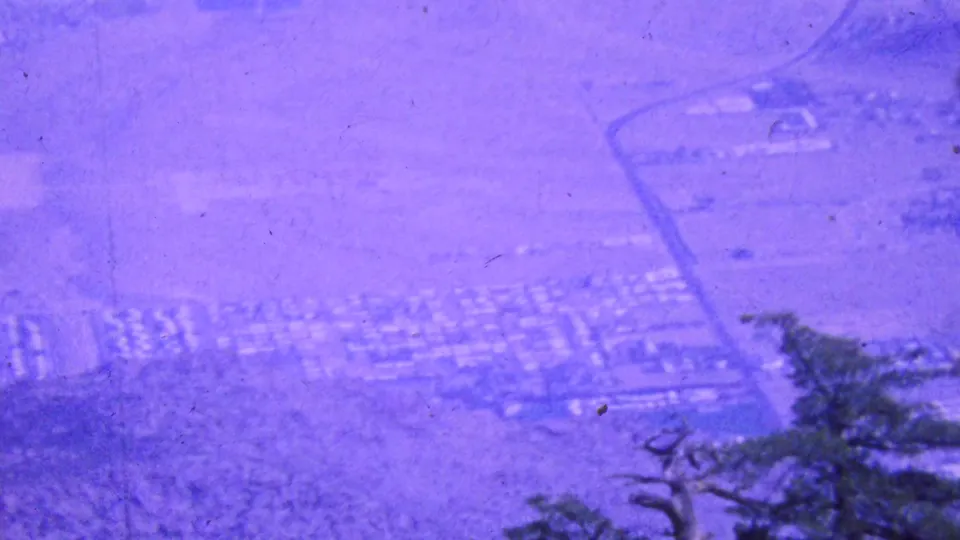 Soft 8mm frame from the Palm Springs tramway area showing desert street patterns, scattered structures, and a dark tree form against the purple-shifted landscape.