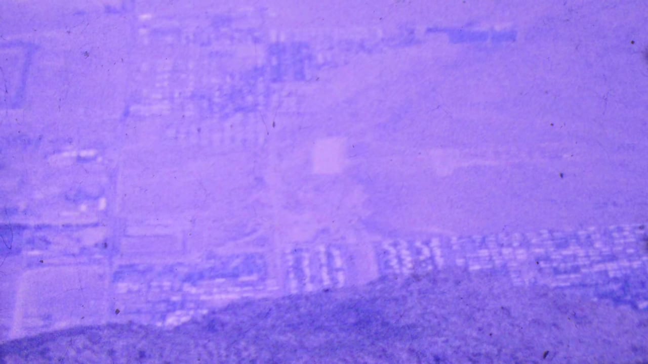 Soft purple-tinted aerial view of roads, housing clusters, and open desert land below.
