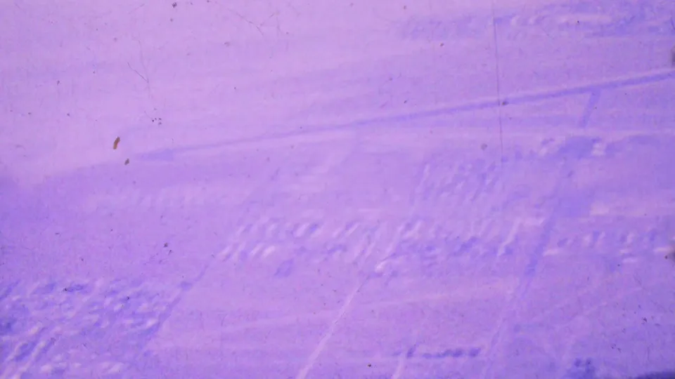A 1964 Palm Springs aerial frame shows pale farmland patterns, faint road lines, and scattered developed areas under a strong purple 8mm color cast.