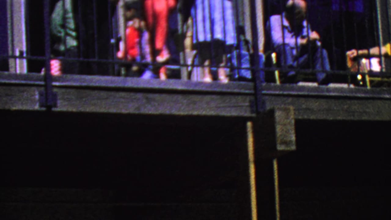 Visitors stand on an upper balcony above a dark exterior structure.