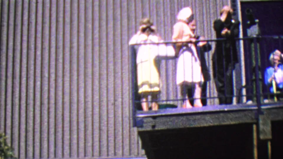 A clearer 1964 Palm Springs Aerial Tramway balcony view shows women in light dresses, a person in dark clothing, and a young girl at the right holding binoculars near the railing.