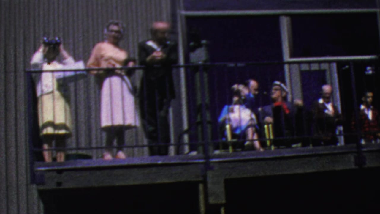 Visitors at the Palm Springs Aerial Tramway balcony look outward and upward, with seated figures, a suited man, and women in period dresses visible.
