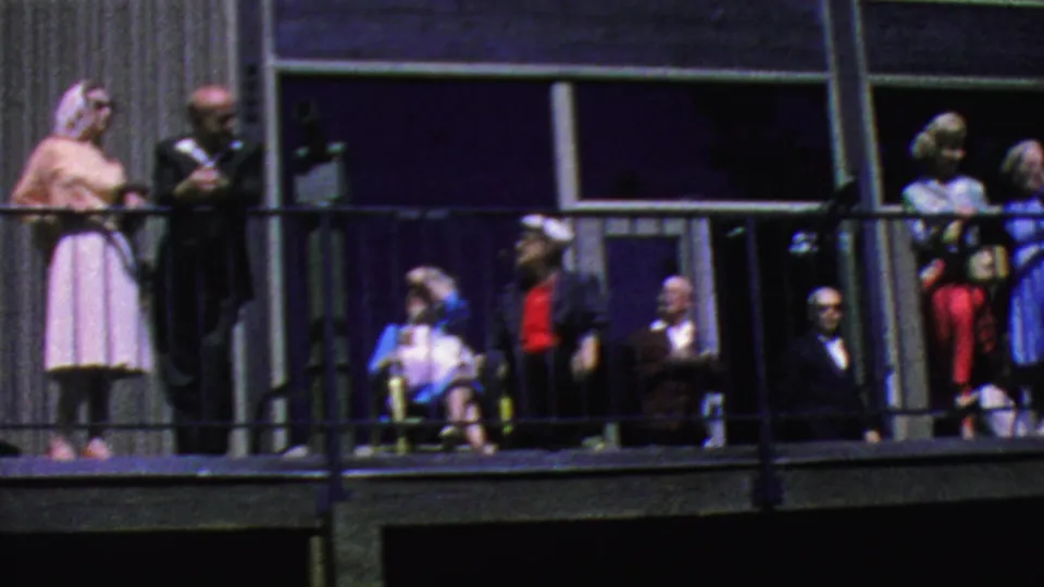 The camera frames more Palm Springs Aerial Tramway visitors along the balcony, including a woman in a pink dress, seated figures, and a person in a red shirt.