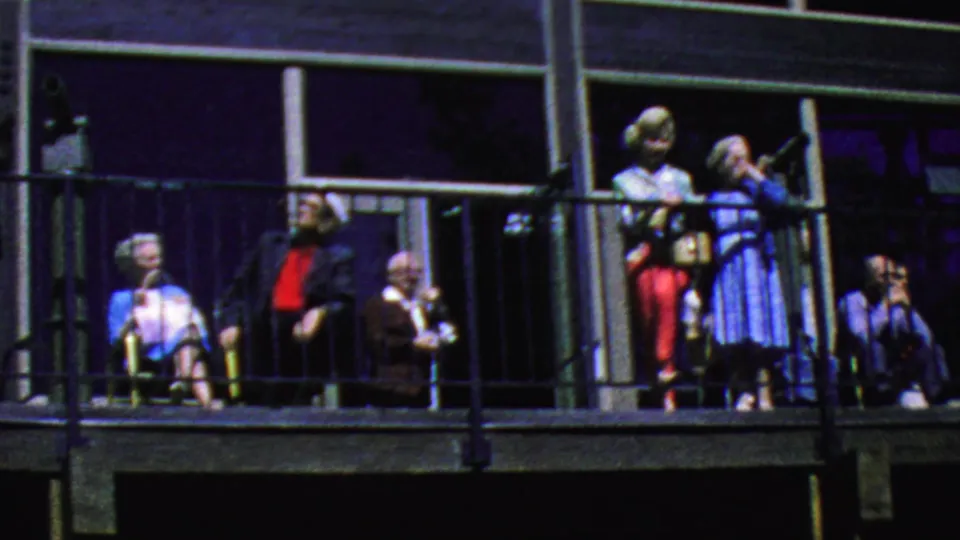 At the Palm Springs Aerial Tramway balcony, visitors in bright mid-century clothing gather near the railing while a seated person at right appears to hold binoculars or a camera.