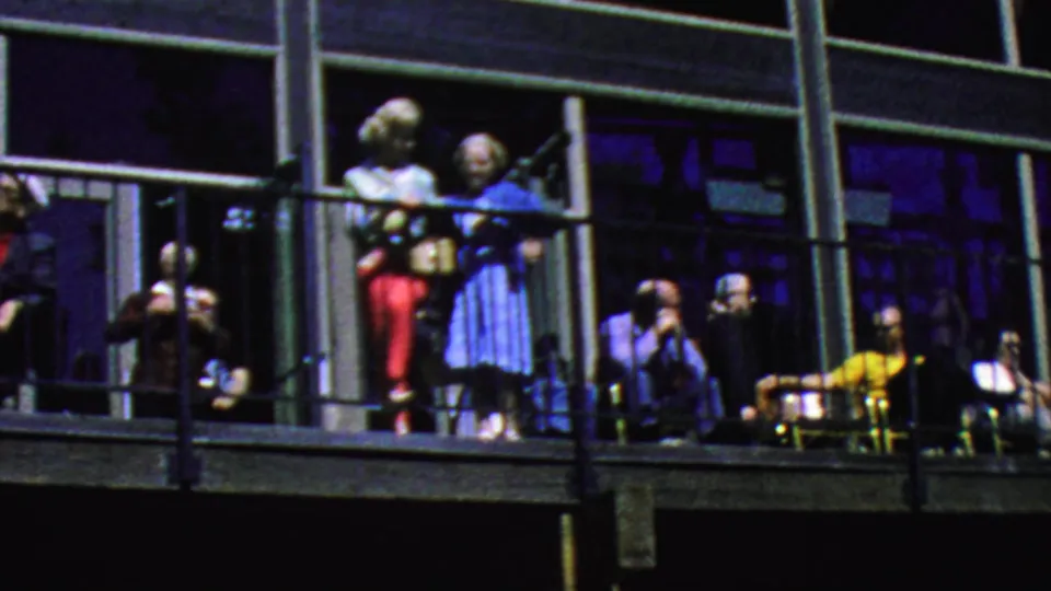 A 1964 Palm Springs balcony view shows adults standing near black railings, including two women near the center and seated visitors beside large dark window bays.