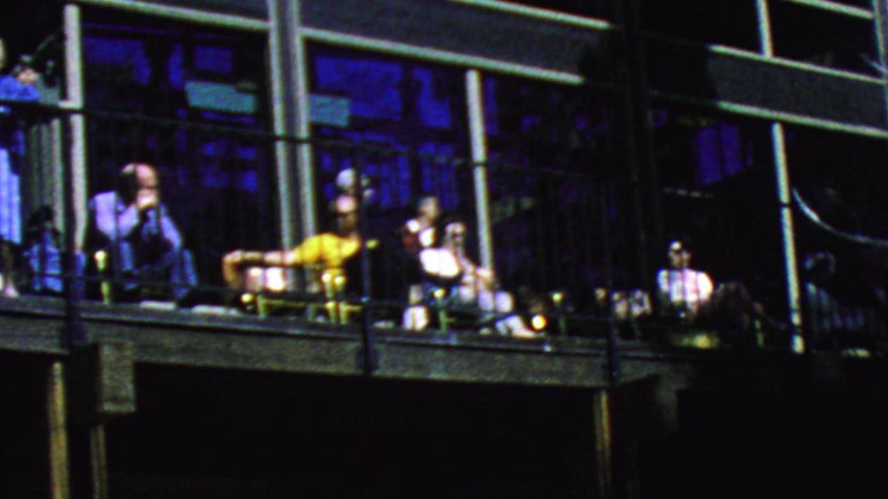 Adults relax on a long balcony at the Palm Springs Aerial Tramway in 1964, with patio chairs, railings, and blue-tinted window reflections visible.