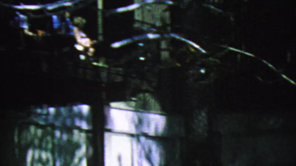The camera drops toward the shaded exterior below the Palm Springs Aerial Tramway balcony, showing tree branches, structural elements, and partial reflections from the deck above.