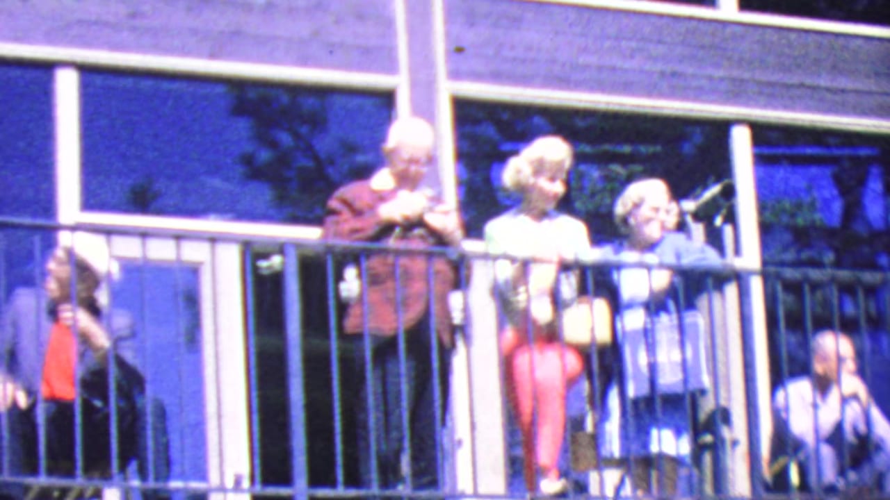 Tourists stand behind a balcony railing while a man raises a camera.