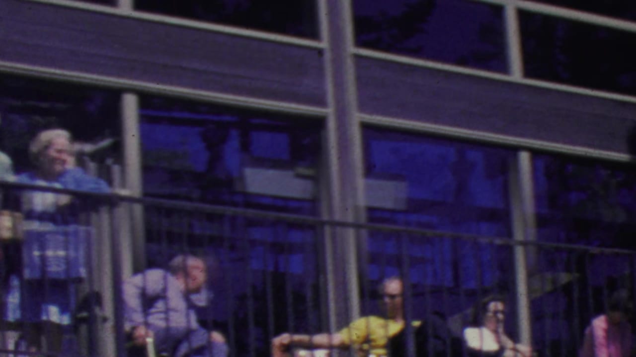 Visitors at the Palm Springs Aerial Tramway sit and stand along a balcony, with a man near the center leaning forward as others watch from behind the railing.
