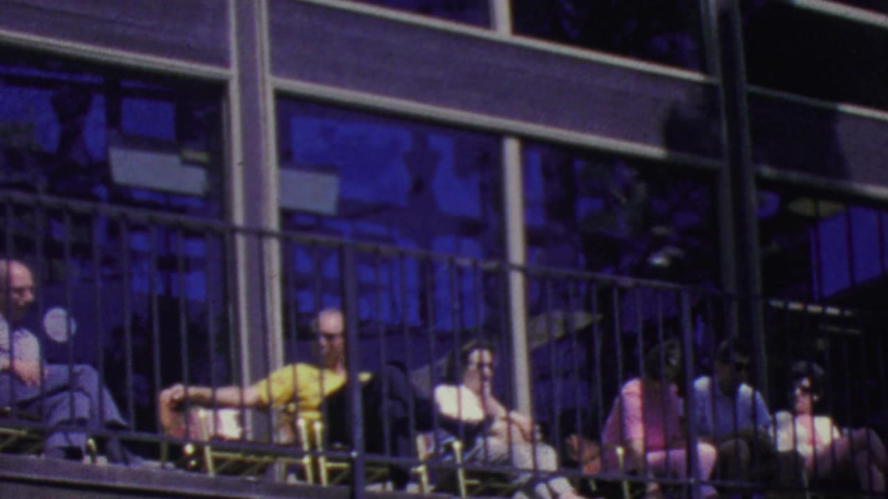 Seated spectators on a balcony watch from behind a dark metal railing.