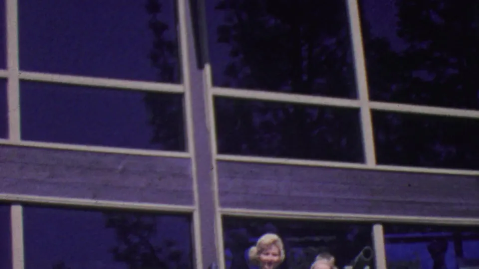 1964 Palm Springs frame showing the glass-and-white-beam exterior with partially visible people near the bottom edge, likely posing in front of the building.