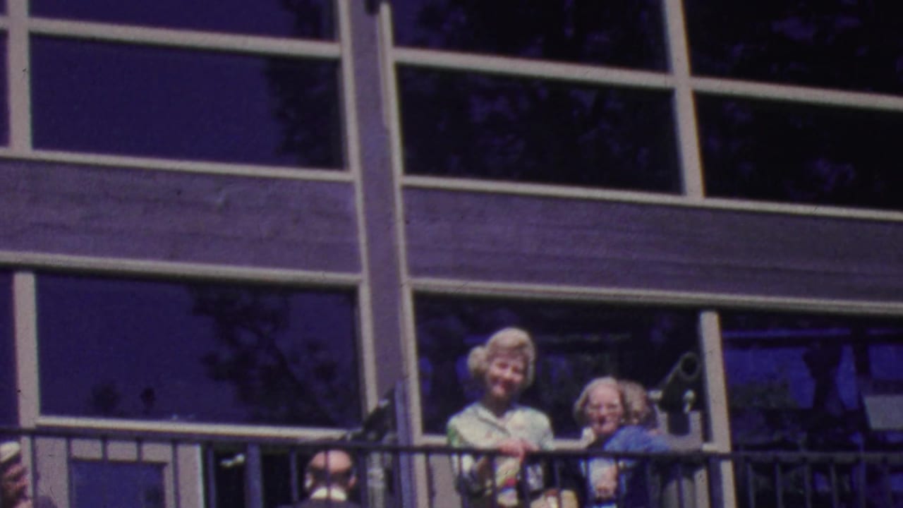 Adults on a balcony outside a modern building with large windows and metal railings.