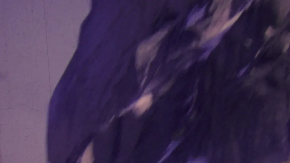 1964 8mm frame from the Palm Springs aerial tramway showing a dark rocky cliff face against a pale lavender sky with visible film scratches and blur.