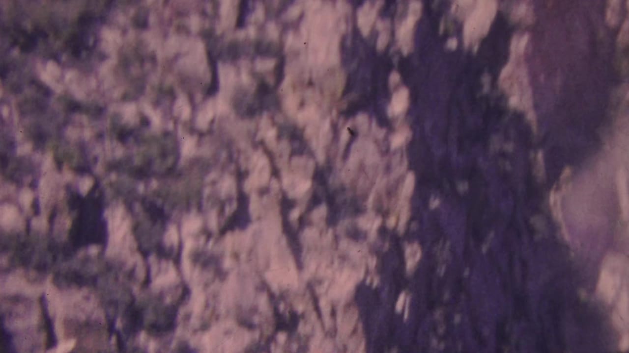 Palm Springs area canyon wall on 1964 8mm film, showing fractured rock formations, sparse desert plants, and mottled sunlight.