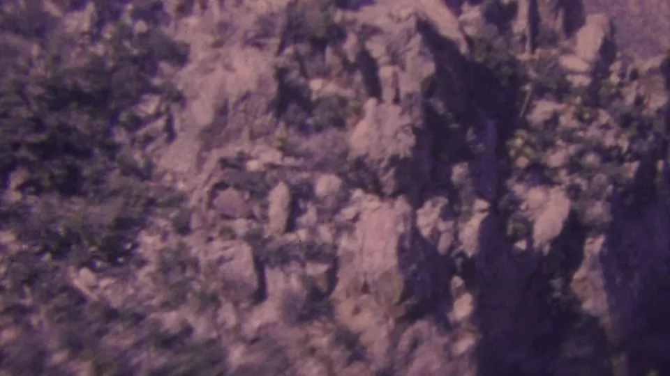 1964 home-movie view of a rugged Palm Springs area canyon slope with rough stone surfaces, sparse shrubs, and heavy shadow areas.