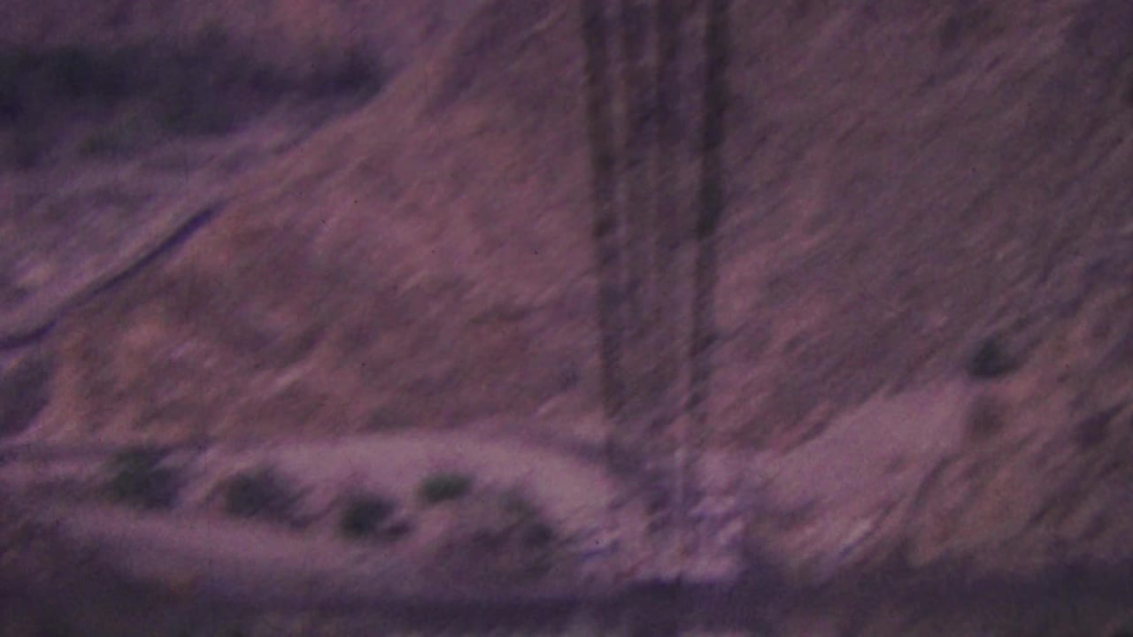 Rocky arid mountain slope with tramway cables and sparse vegetation.