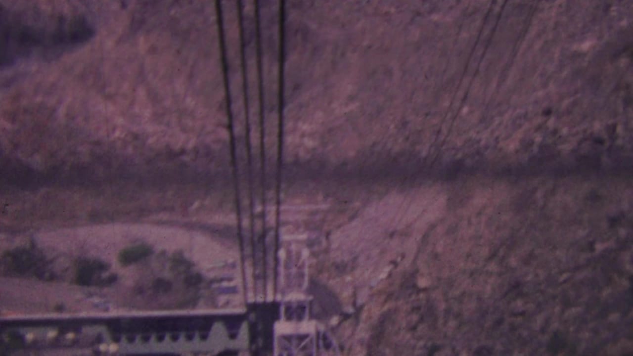 High-angle 1964 Palm Springs tramway view with dark cables crossing a faded desert canyon and a metal support tower below.